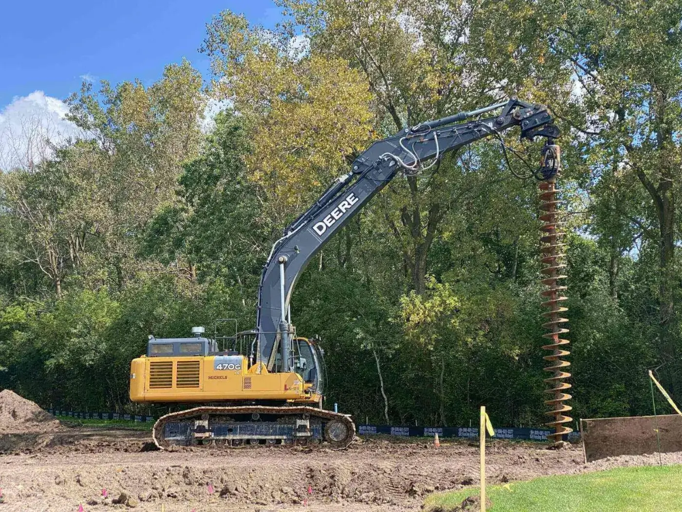 A yellow excavator with a large drilling attachment at a construction site.